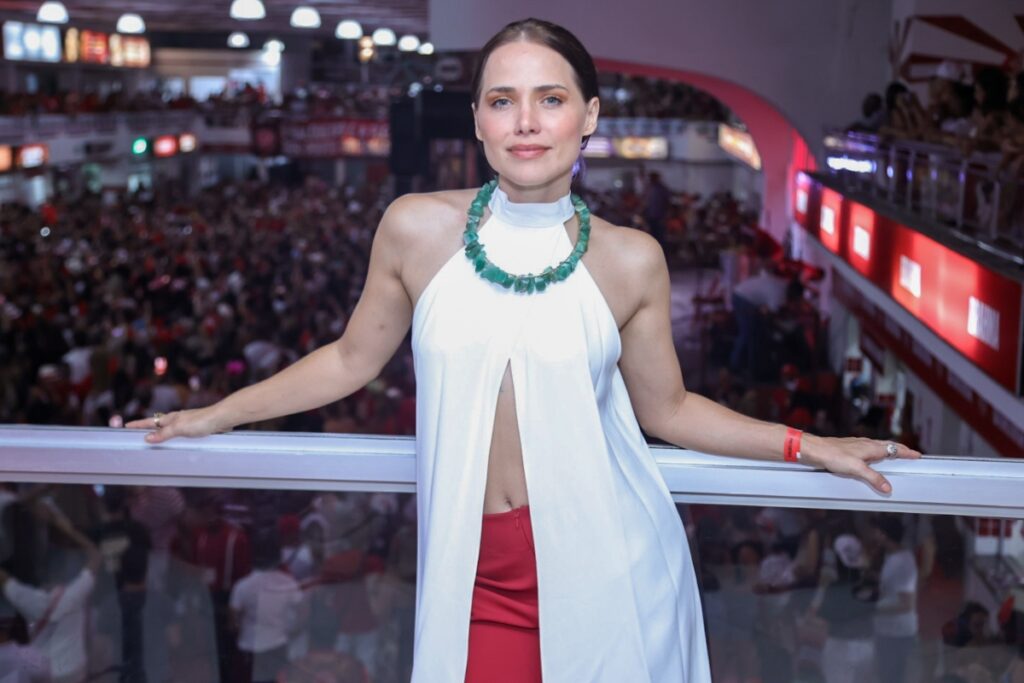 Carnaval RJ - Letíicia Collin de camisa branca com fenda frontal, exibindo a barriga, e calça vermelha, colar verde, na quadra do Salgueiro